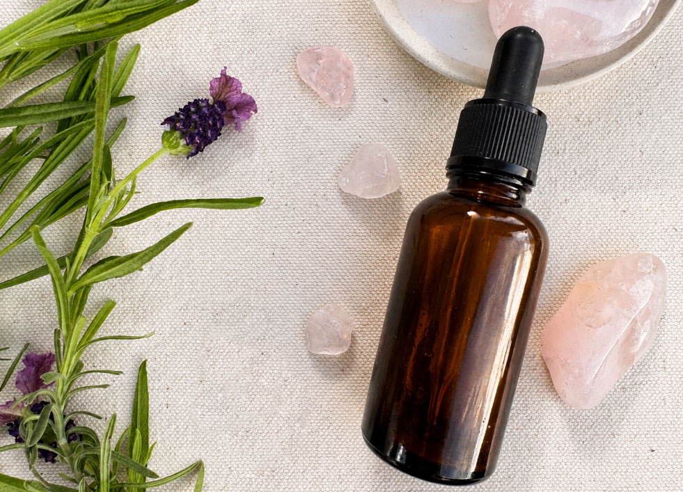 Amber glass dropper bottle surrounded by rose quartz crystals and lavender on natural linen fabric in soft sunlight